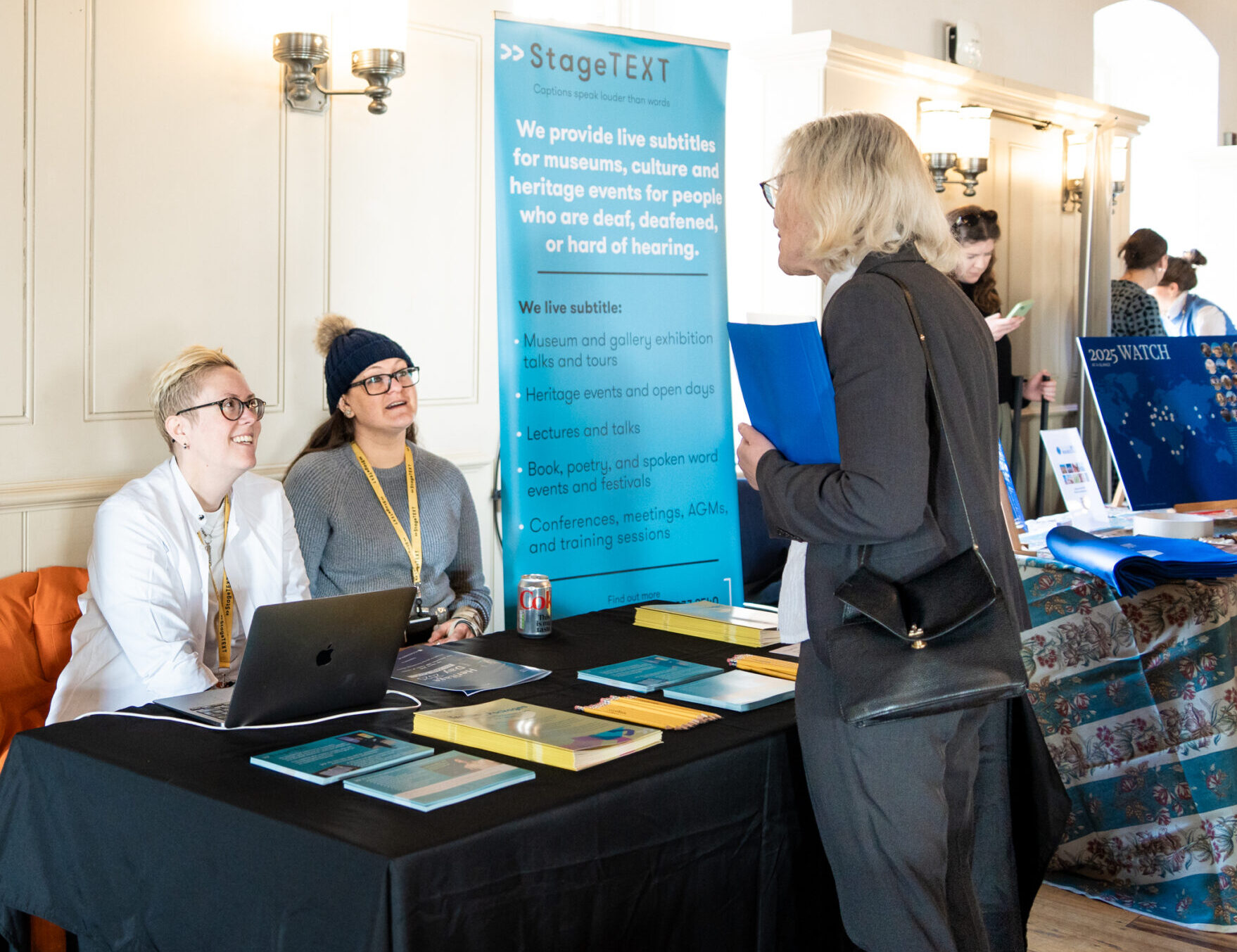 Stagetext staff members Hannah and Courtney speaking to Chair of the Heritage Alliance, Carole Souter CBE at the Heritage Day 2025